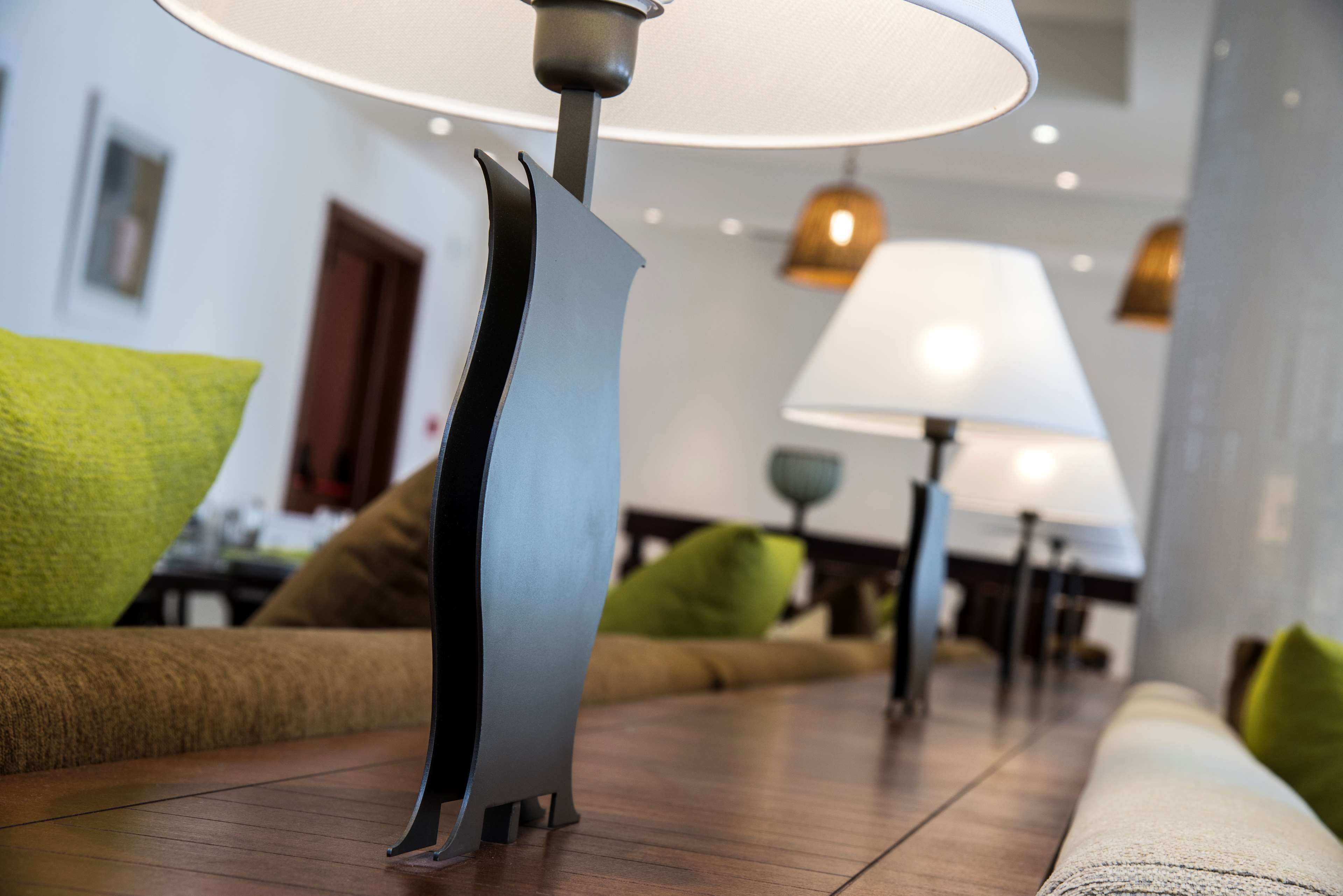 Una sala moderna con suelo de madera, un sofá con cojines verdes y una lámpara con pantalla blanca.