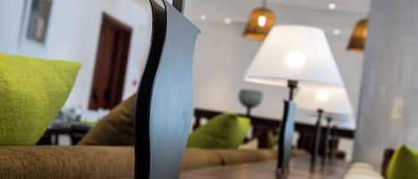 Una sala moderna con suelo de madera, un sofá con cojines verdes y una lámpara con pantalla blanca.