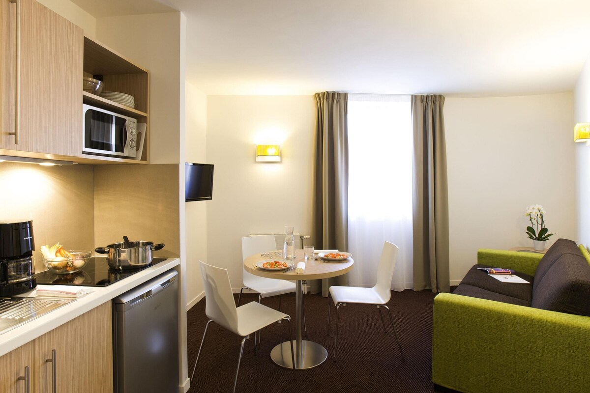 Habitación de hotel compacta con kitchenette, comedor, sofá y televisor.
