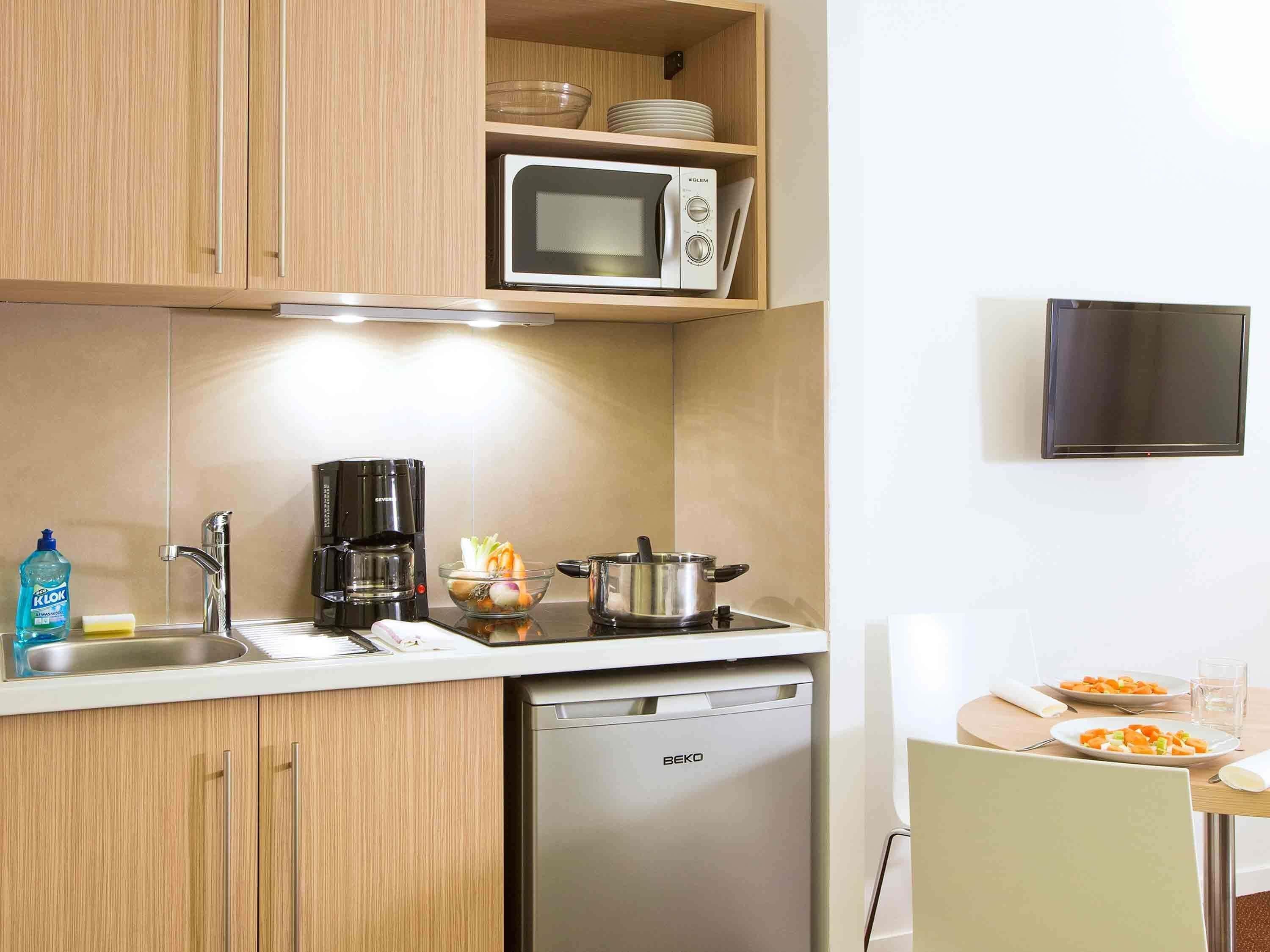 Een kleine keuken met houten kastjes, een magnetron, koffiezetapparaat, spoelbak en vaatwasser.
