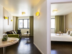 A hotel room with a green sofa, a small round table with a laptop, a bed with a bedside table, and a window with curtains. - Aparthotel Adagio Access Paris Reuilly (Paris)