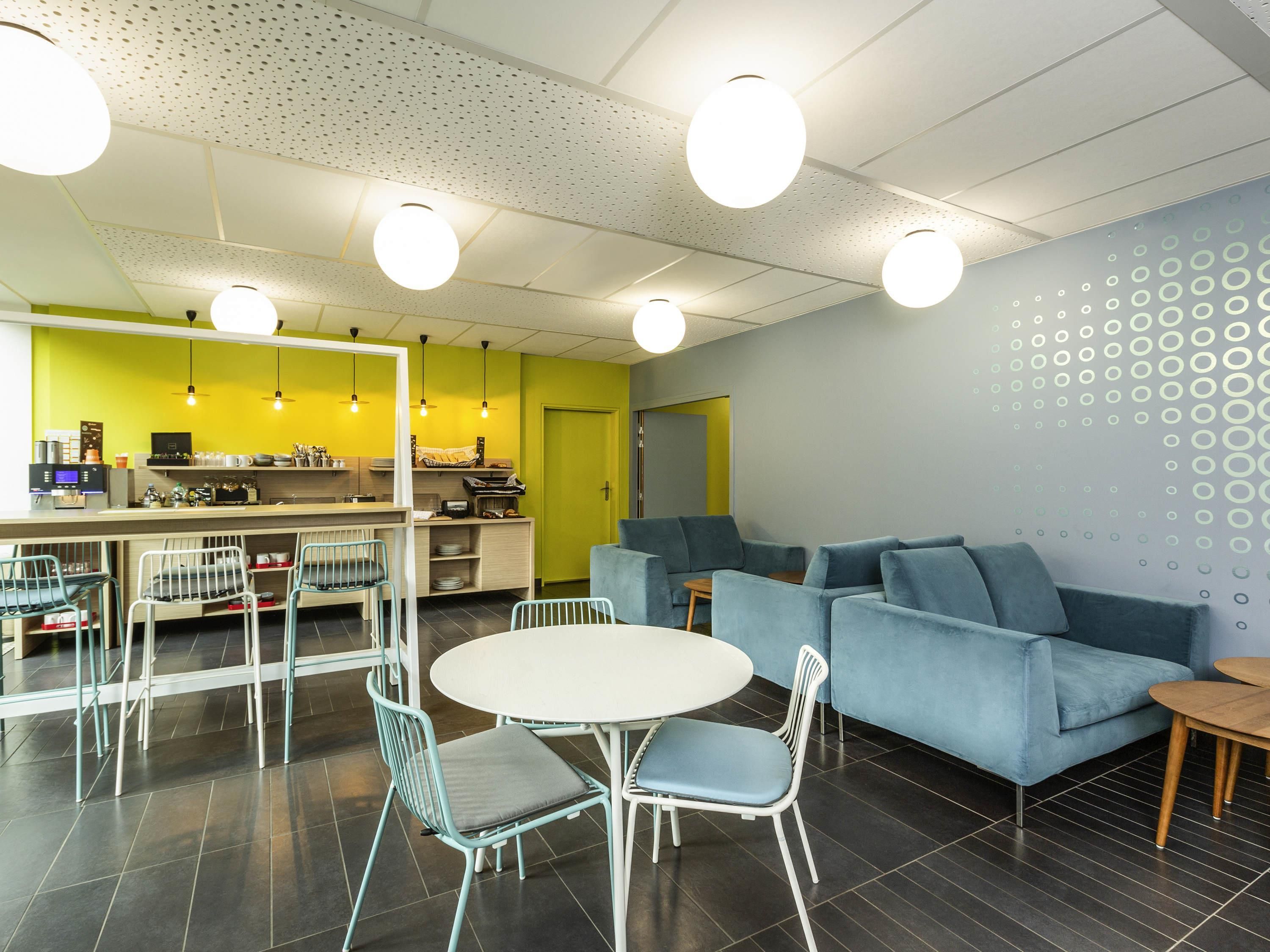 A modern dining area with a round table, chairs, a sofa, and a kitchen in the background.