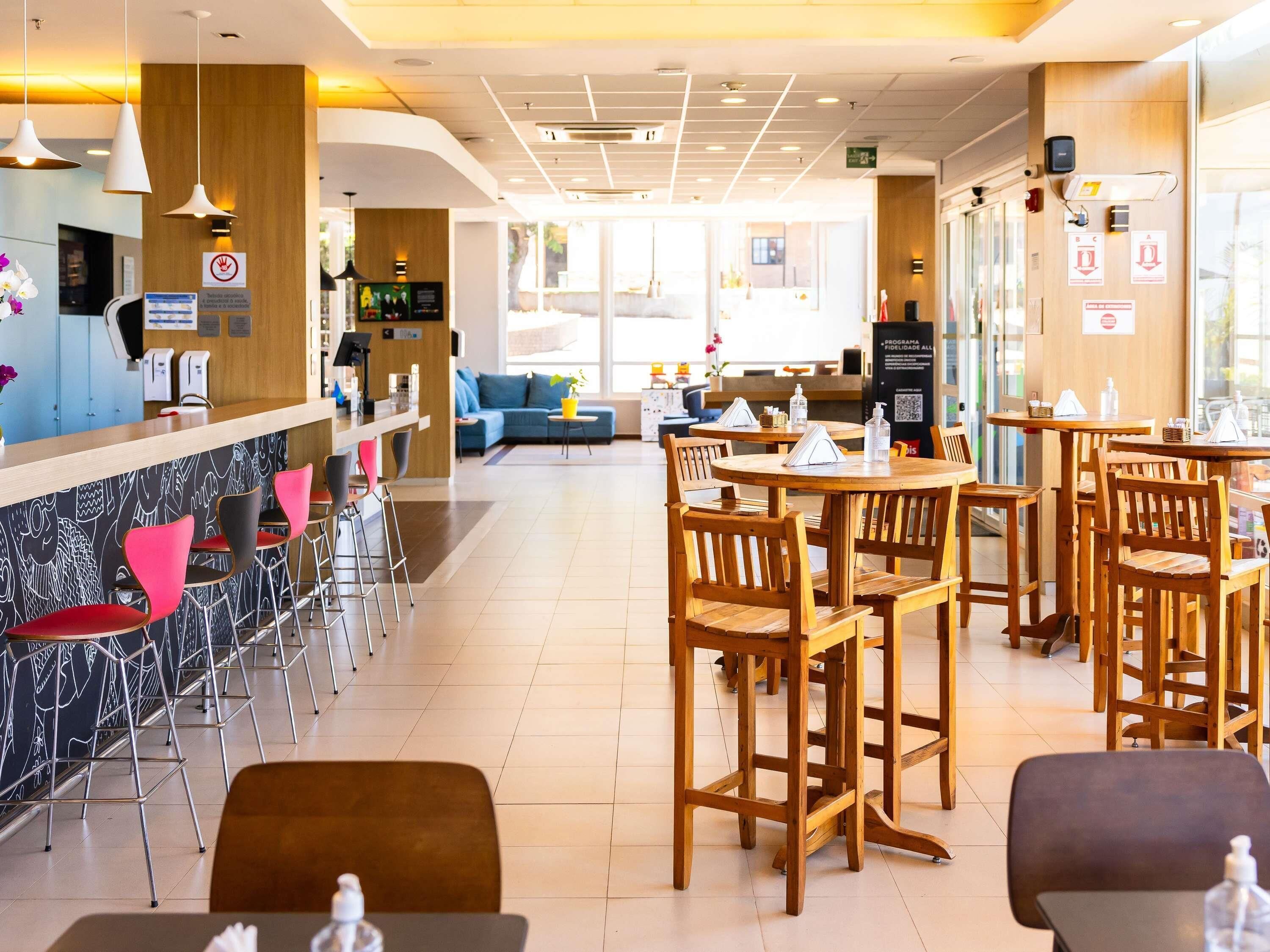 A modern cafe with a bar area, wooden tables and chairs, and a seating area with sofas.