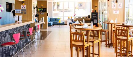 A modern cafe with a bar area, wooden tables and chairs, and a seating area with sofas.