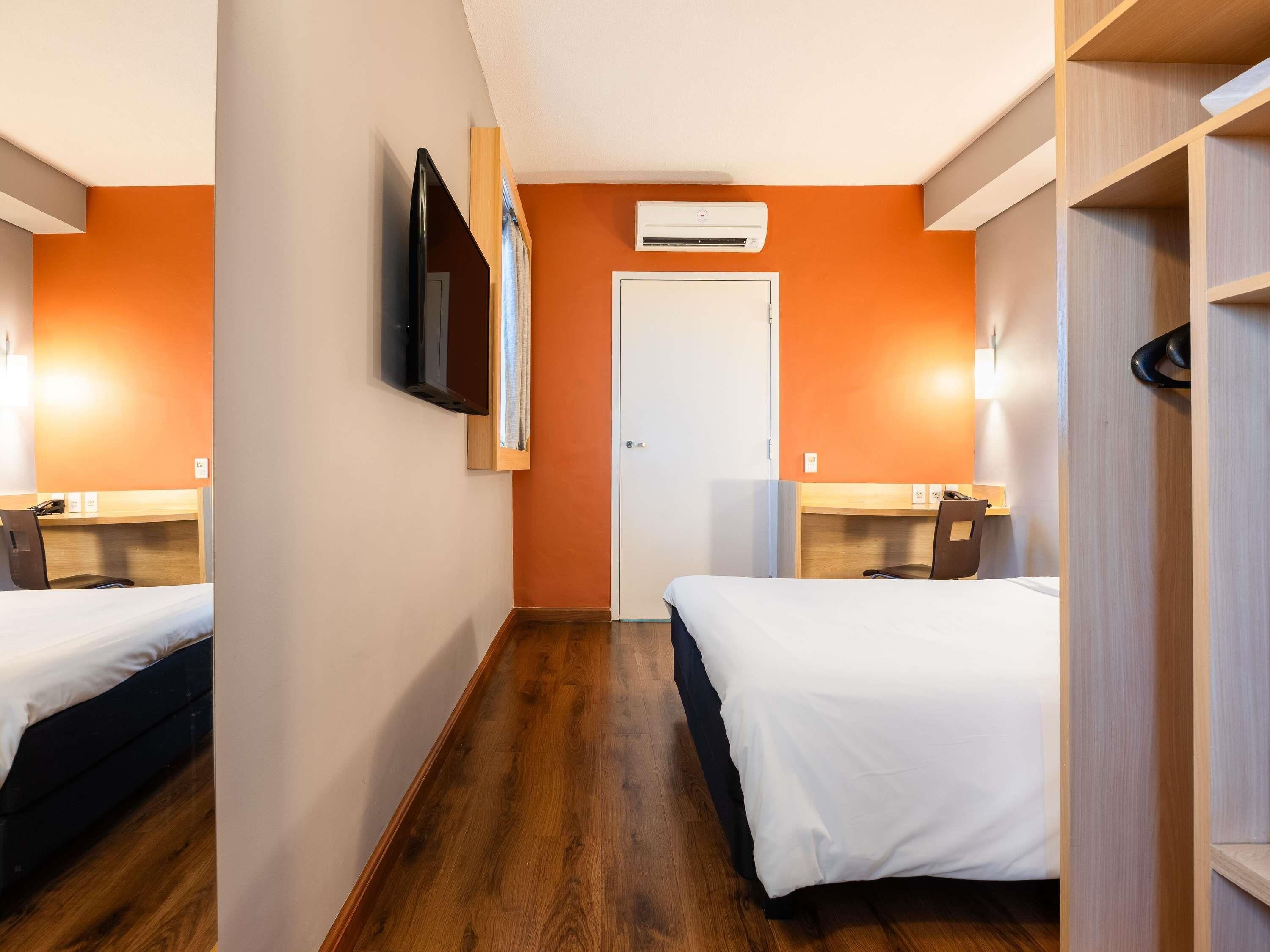A hotel room with two beds, a TV, an air conditioning unit, and a wooden floor.