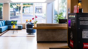 A modern hotel lobby with a reception desk, seating area, and large windows offering a view of the street. - ibis Ourinhos (Ourinhos)