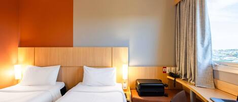 Habitación de hotel con dos camas, un escritorio con una computadora portátil, una silla, una maleta y un par de audífonos.