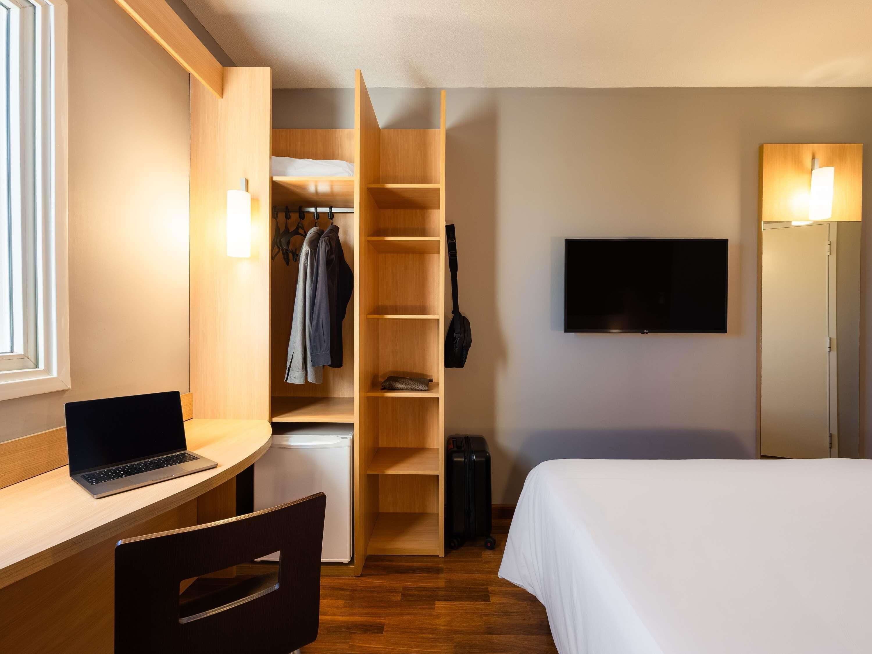 Habitación de hotel con escritorio, computadora portátil, cama, televisor y vestidor.