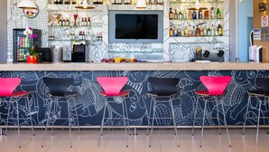 A bar area with a counter, bar stools, a TV screen, and shelves of bottles. - ibis Ourinhos (Ourinhos)