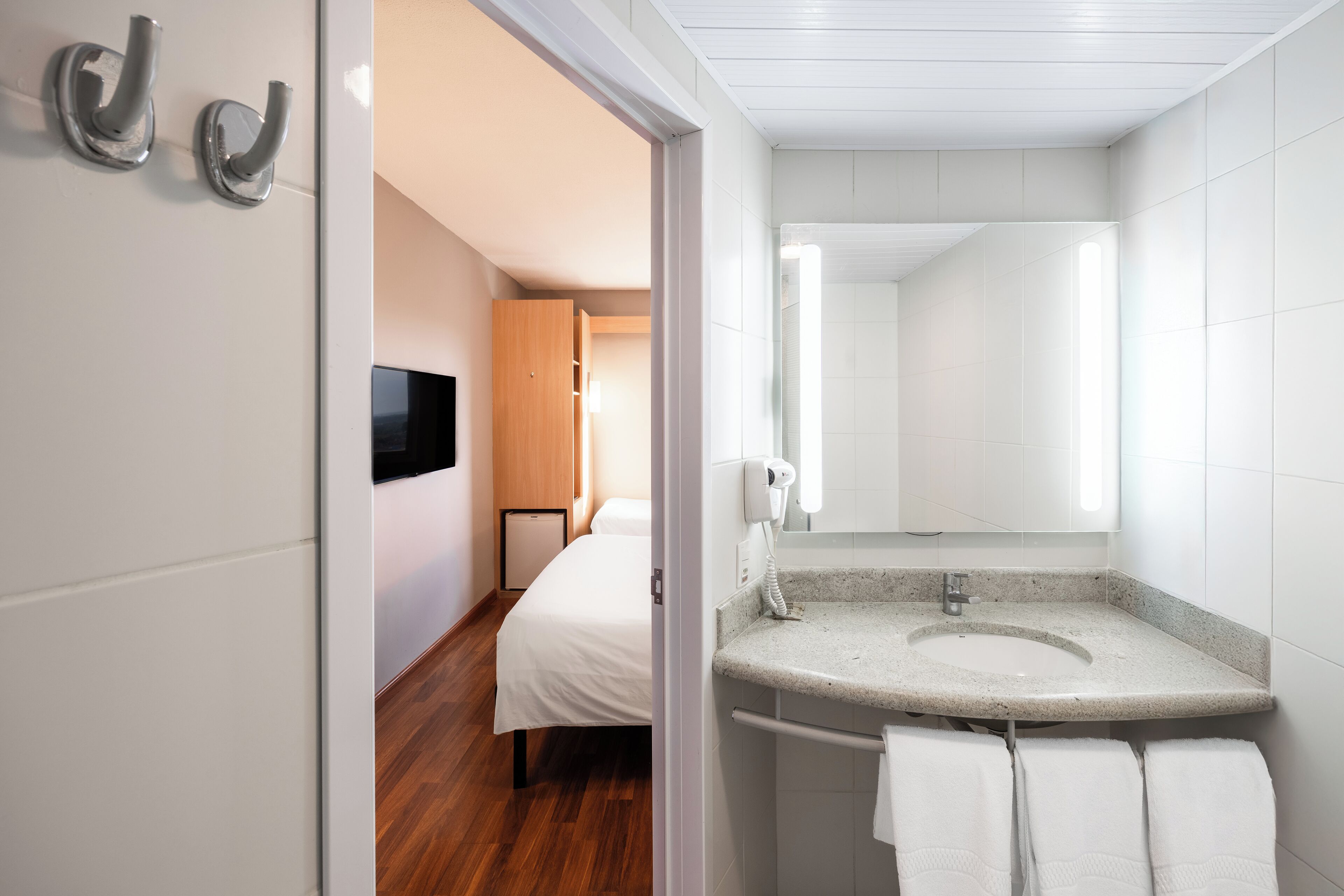 Ein modernes Hotelbad mit einem Granittisch, weißen Fliesen und einer Duschkabine.
