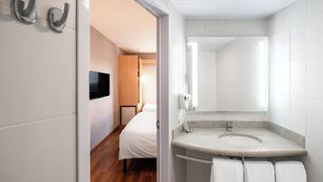 Ett modernt hotellbadrum med en diskho i granit, vita kakelplattor och en duschhörna.