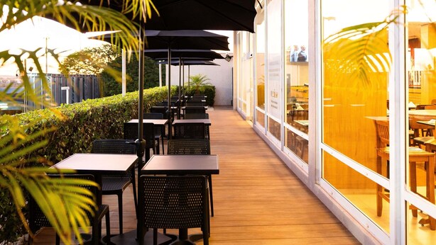 An outdoor seating area with tables and chairs, umbrellas, and a view of the interior through large windows. - ibis Ourinhos (Ourinhos)