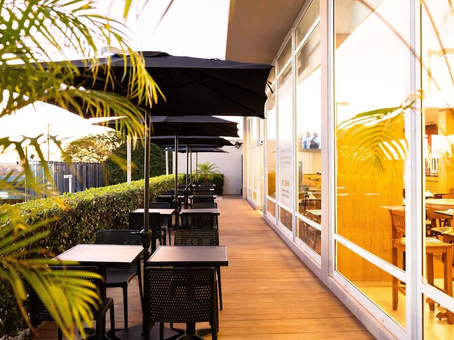 Een terras met tafels en stoelen, parasols en uitzicht op het interieur door grote ramen.