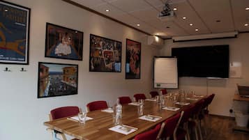 A conference room with a long table, red chairs, and various posters on the walls.