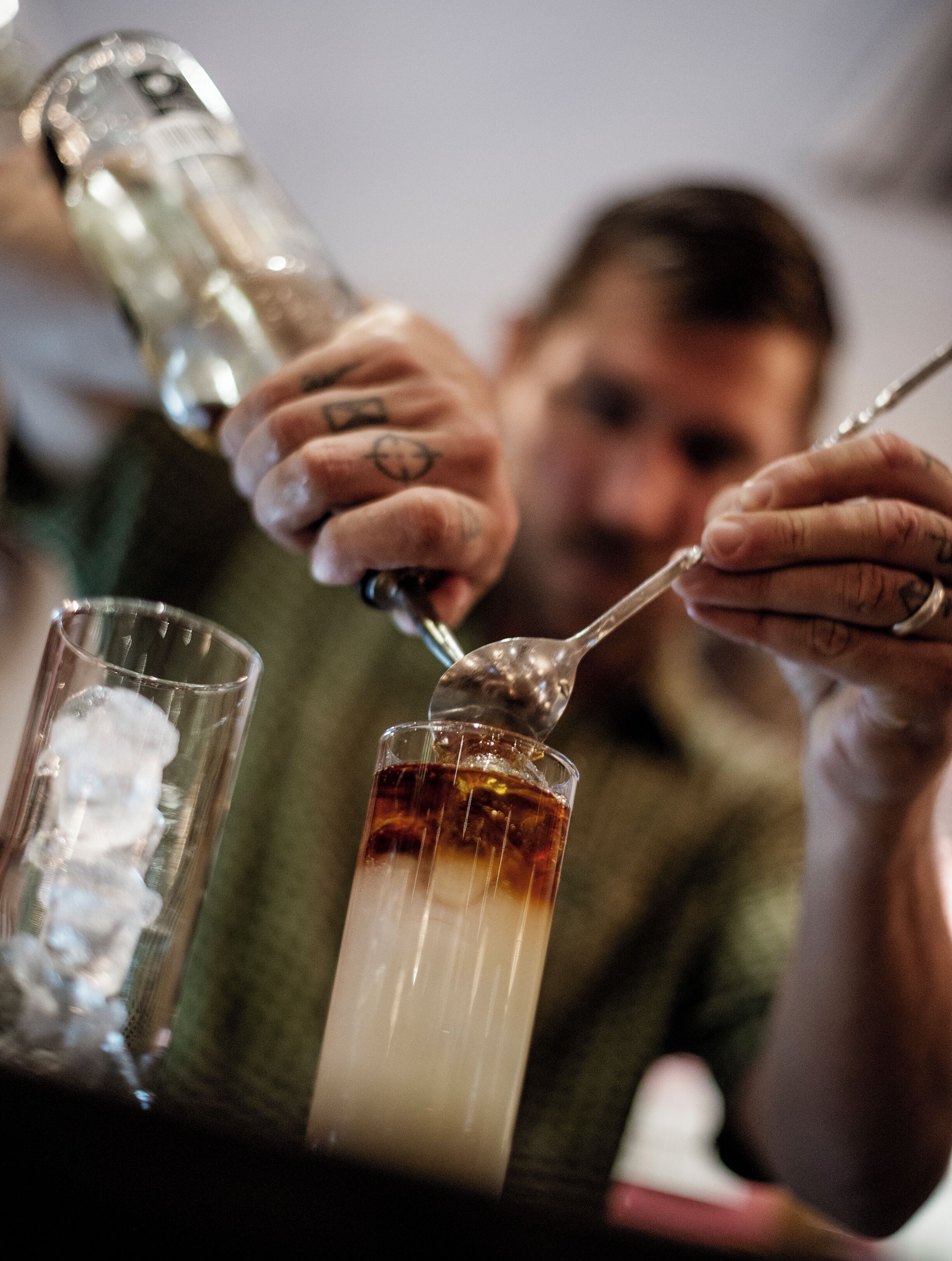 A person pouring a dark liquid into a glass with ice cubes.