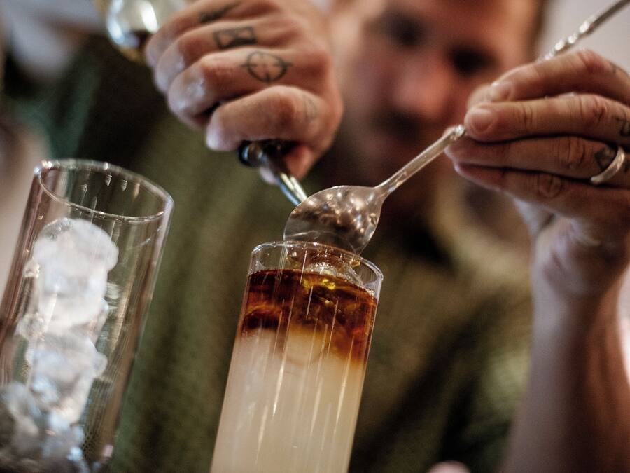 A person pouring a dark liquid into a glass with ice cubes.