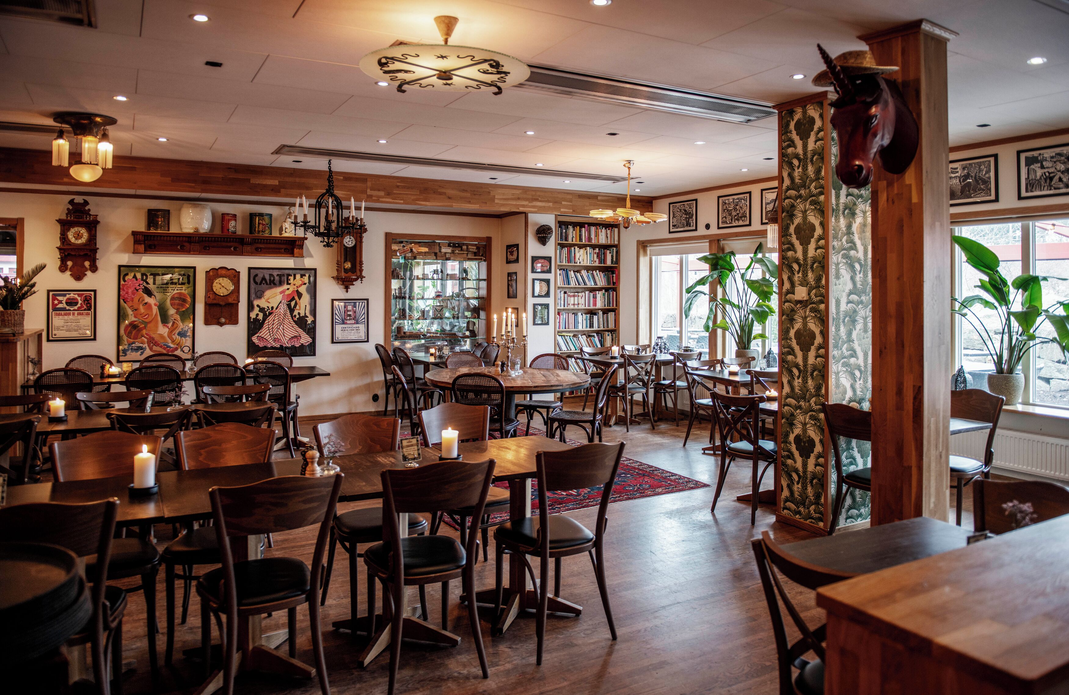 A restaurant with wooden tables and chairs, a chandelier, and a bookshelf filled with books.