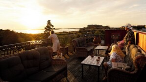 Una terraza con mobiliario de mimbre, una mesa y vistas al atardecer sobre el agua.