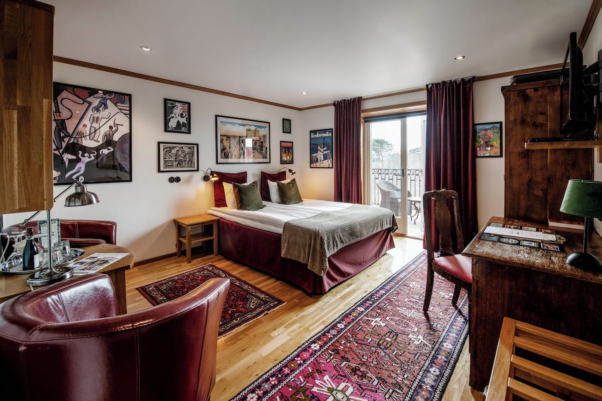 A bedroom with a large bed, a desk, a chair, and a balcony.