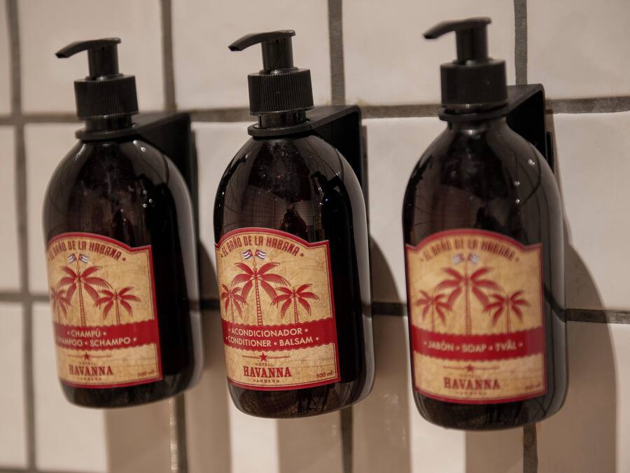 Three bottles of Havana hotel brand toiletries mounted on a tiled wall.