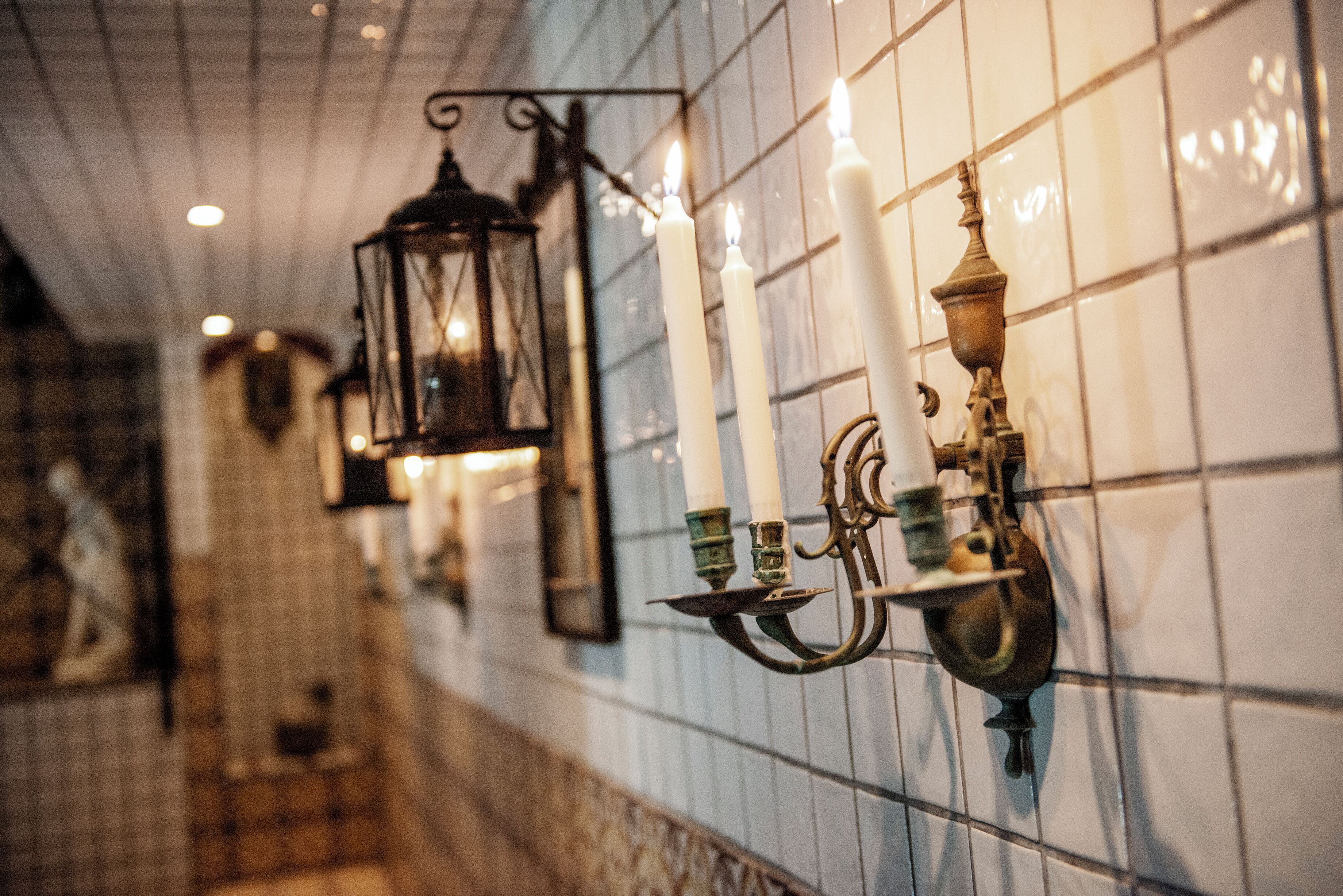 A corridor with tiled walls, a hanging lantern, and wall-mounted candle holders.