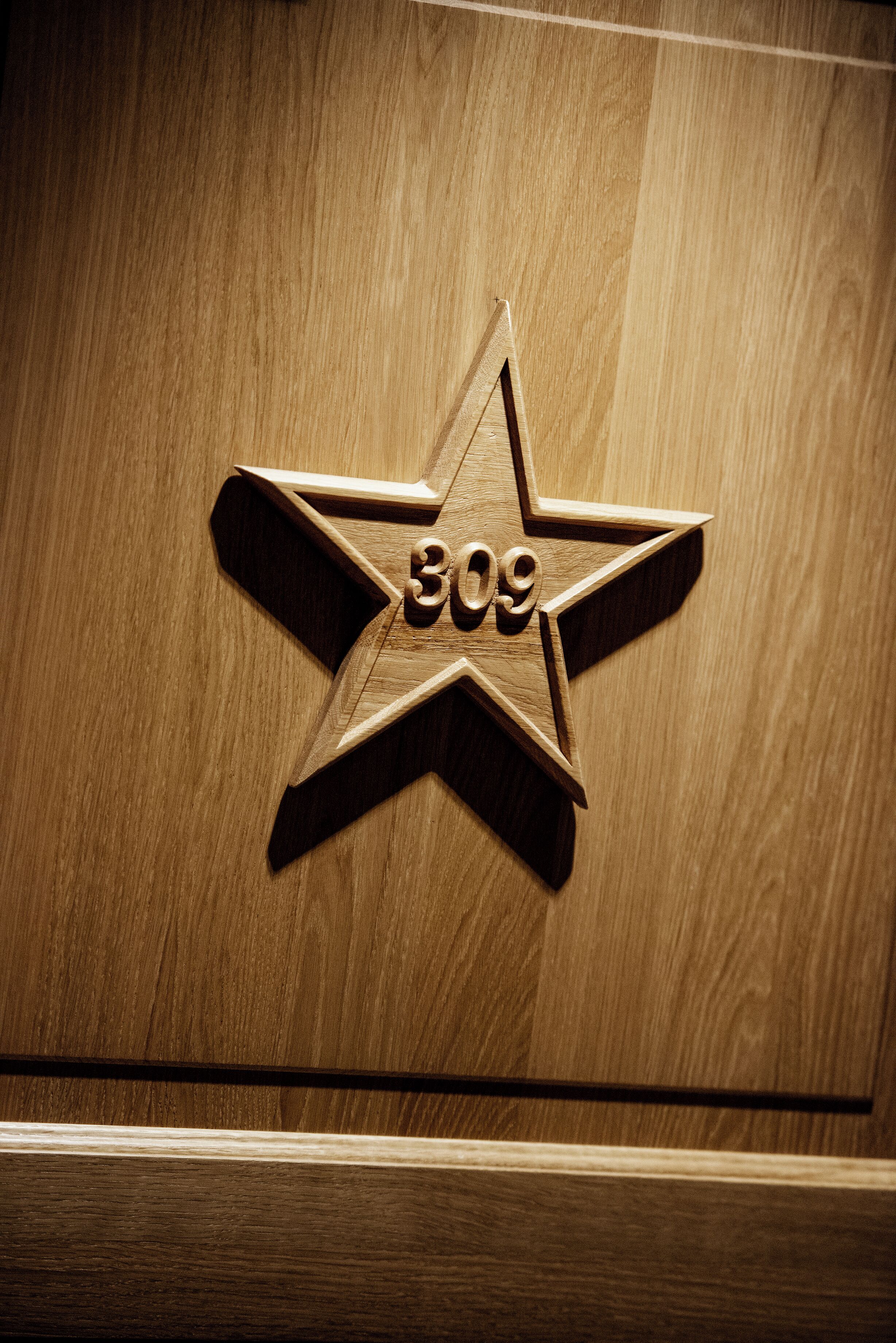 A wooden star-shaped plaque with the number 309 on a wooden surface.