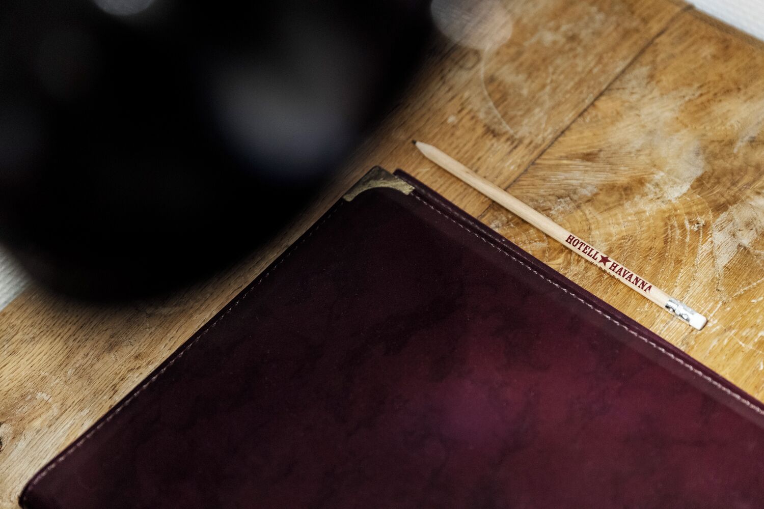 Una superficie di legno con un oggetto in pelle rosso scuro e un bastoncino di legno con del testo.