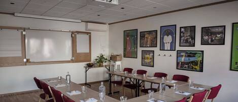 A conference room with a long table, red chairs, a projector, and artwork on the walls.
