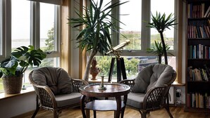 Una habitación acogedora con suelo de madera, dos sillones cómodos, una mesa redonda y una estantería.