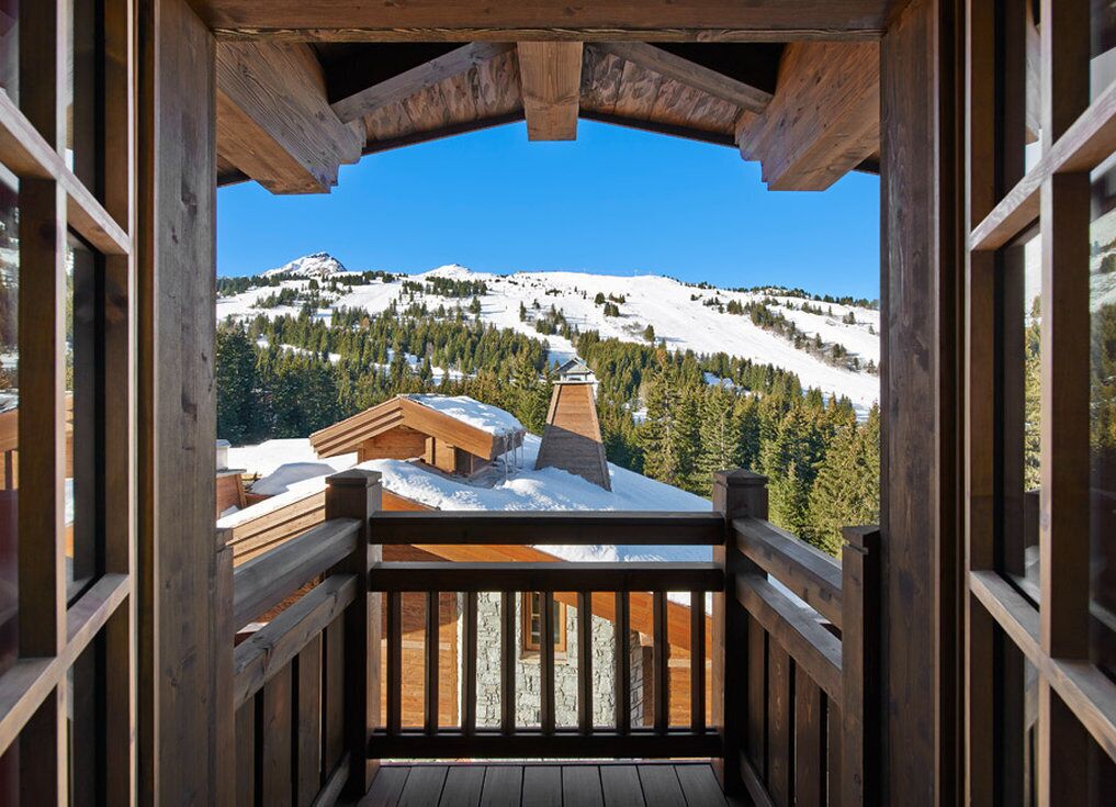 A wooden balcony with a view of a snow-covered mountain and a ski resort.