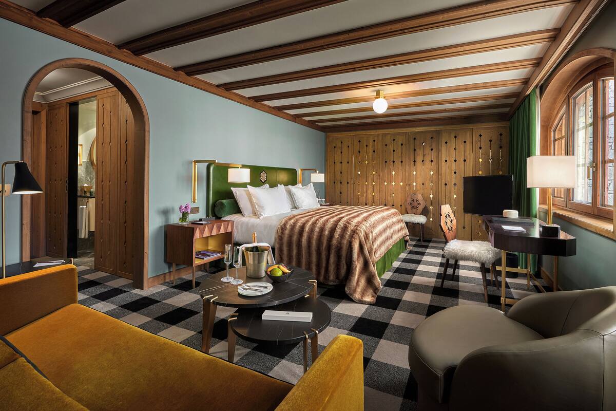 Ein Hotelzimmer mit Schachbrettmuster-Boden, einem Bett mit grünem Kopfteil, einem Schreibtisch mit Computer und einem Stuhl.