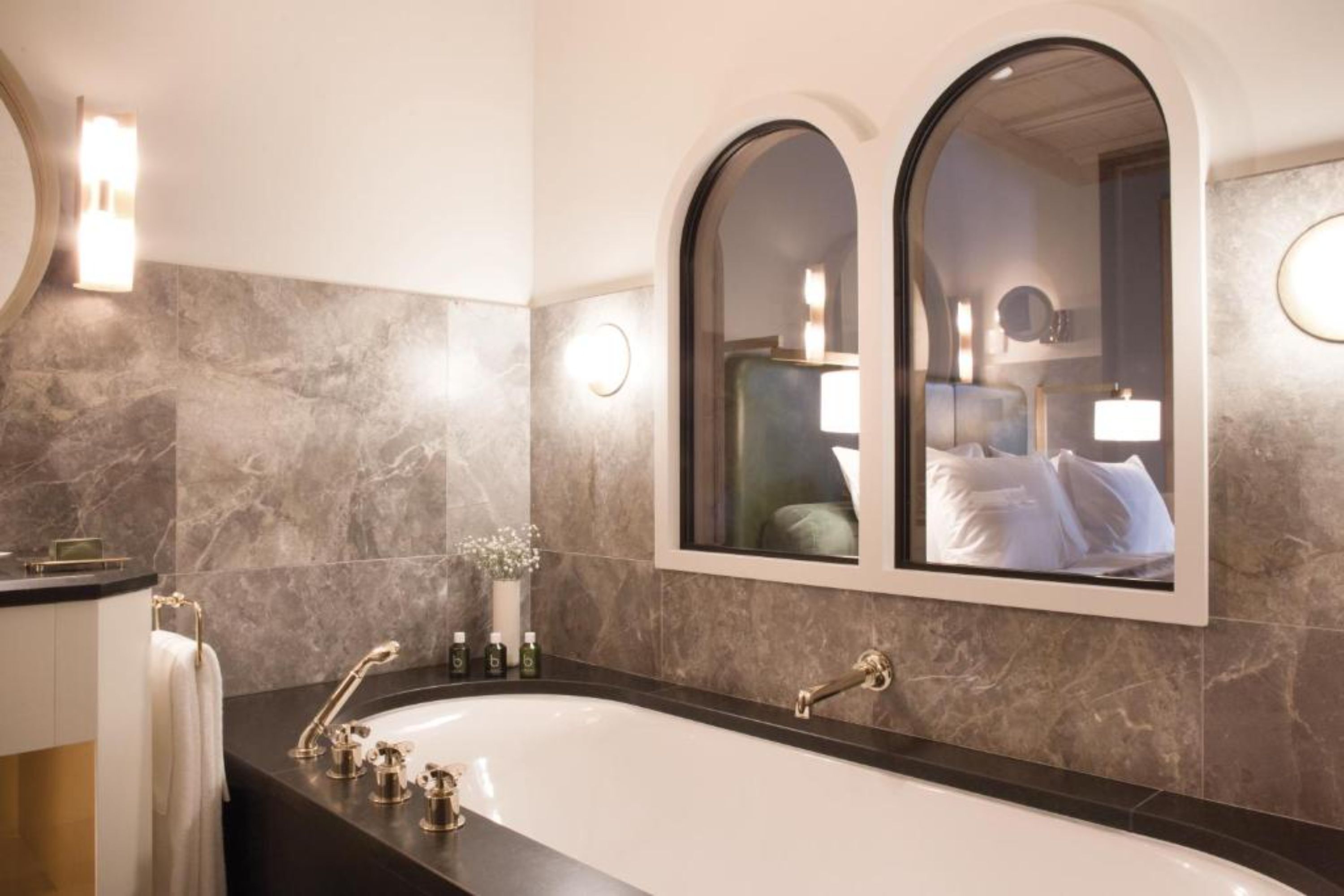 A modern bathroom with a large freestanding bathtub, a vanity with a mirror, and marble walls.