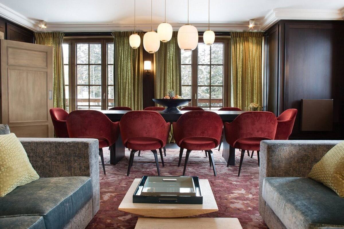 Ein Essbereich mit Tisch und Stühlen, einer Chandelierleuchtre und Blick auf Bäume durch große Fenster.