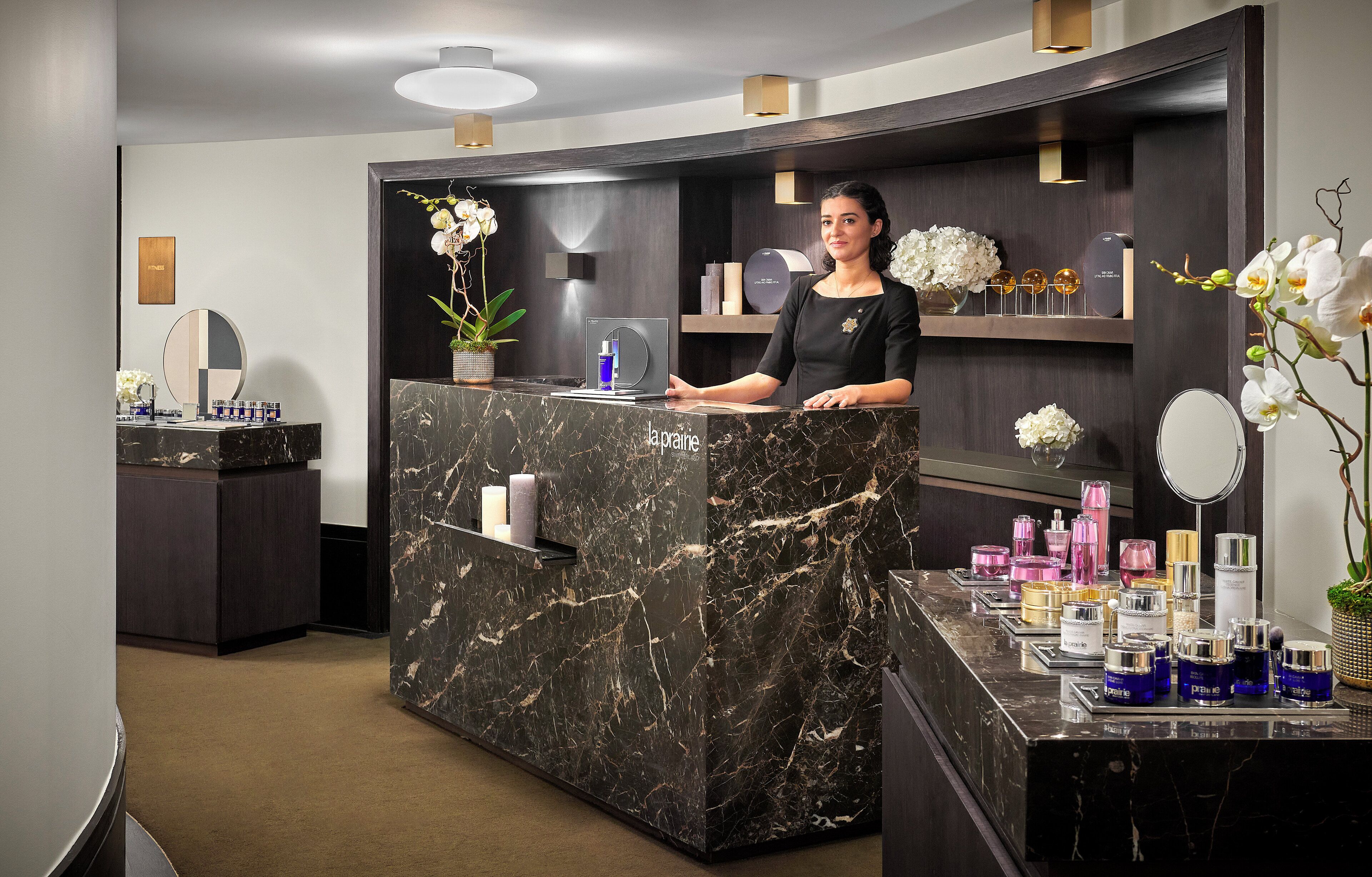 Una moderna recepción con mostrador de mármol, estantes con productos y orquídeas decorativas.