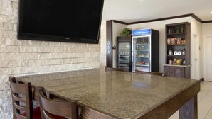 Un área de cocina con encimera de granito, un televisor de pantalla plana montado en la pared, un refrigerador y una despensa con estantes.