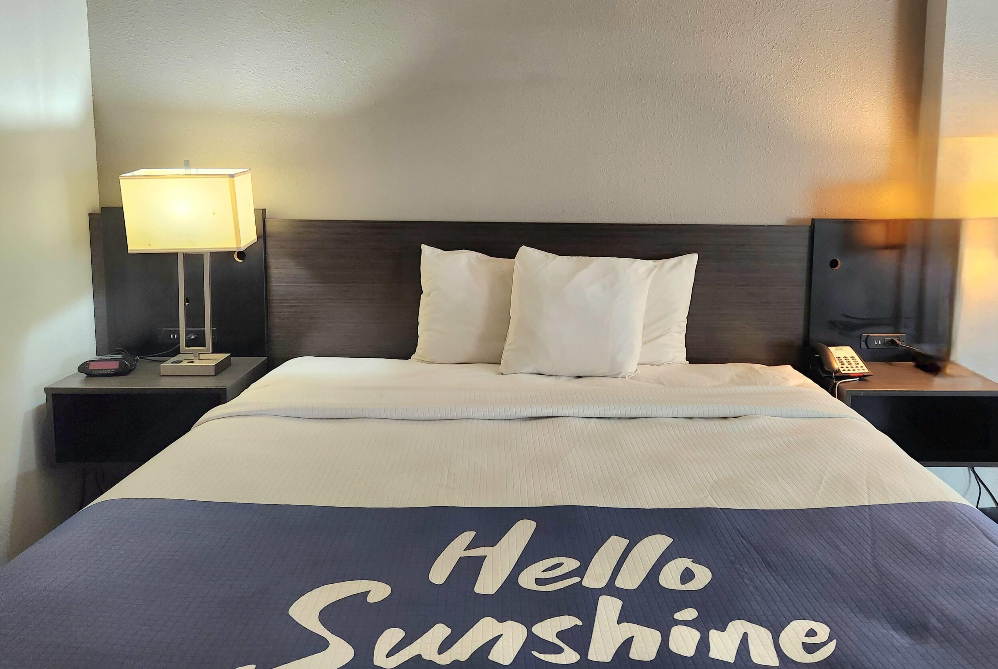 Habitación de hotel con una cama, dos mesitas de noche, una lámpara y un teléfono junto a la cama.