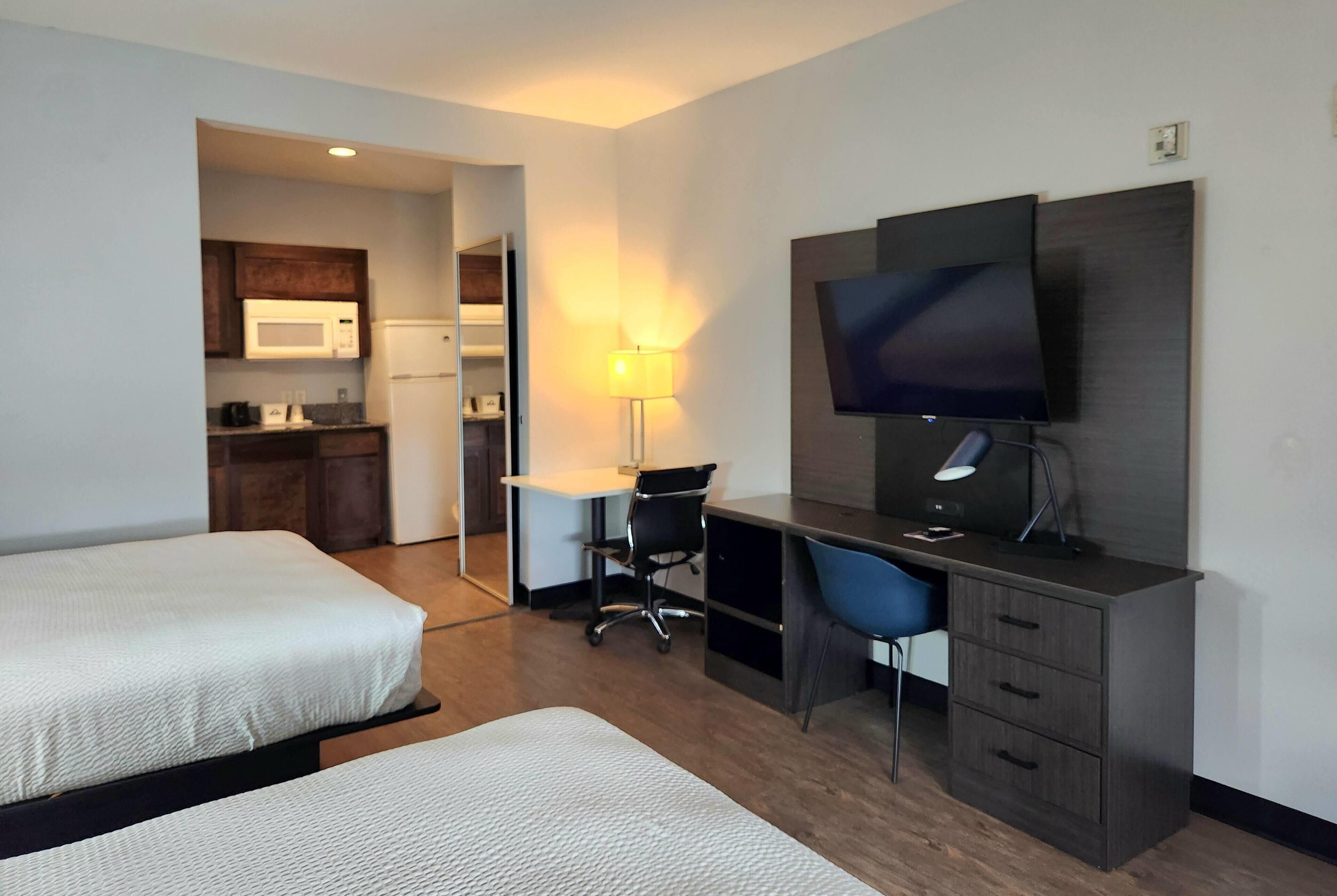 Une chambre d’hôtel avec deux lits, un bureau, une chaise, une télévision et une kitchenette.