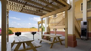 Un espacio al aire libre techado con mesas de picnic, una parrilla y una escalera que lleva a un nivel superior.