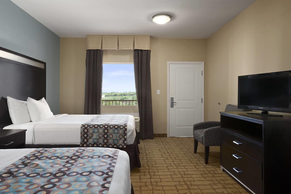 Quarto de hotel com duas camas, televisão, escrivaninha e vista para o exterior.