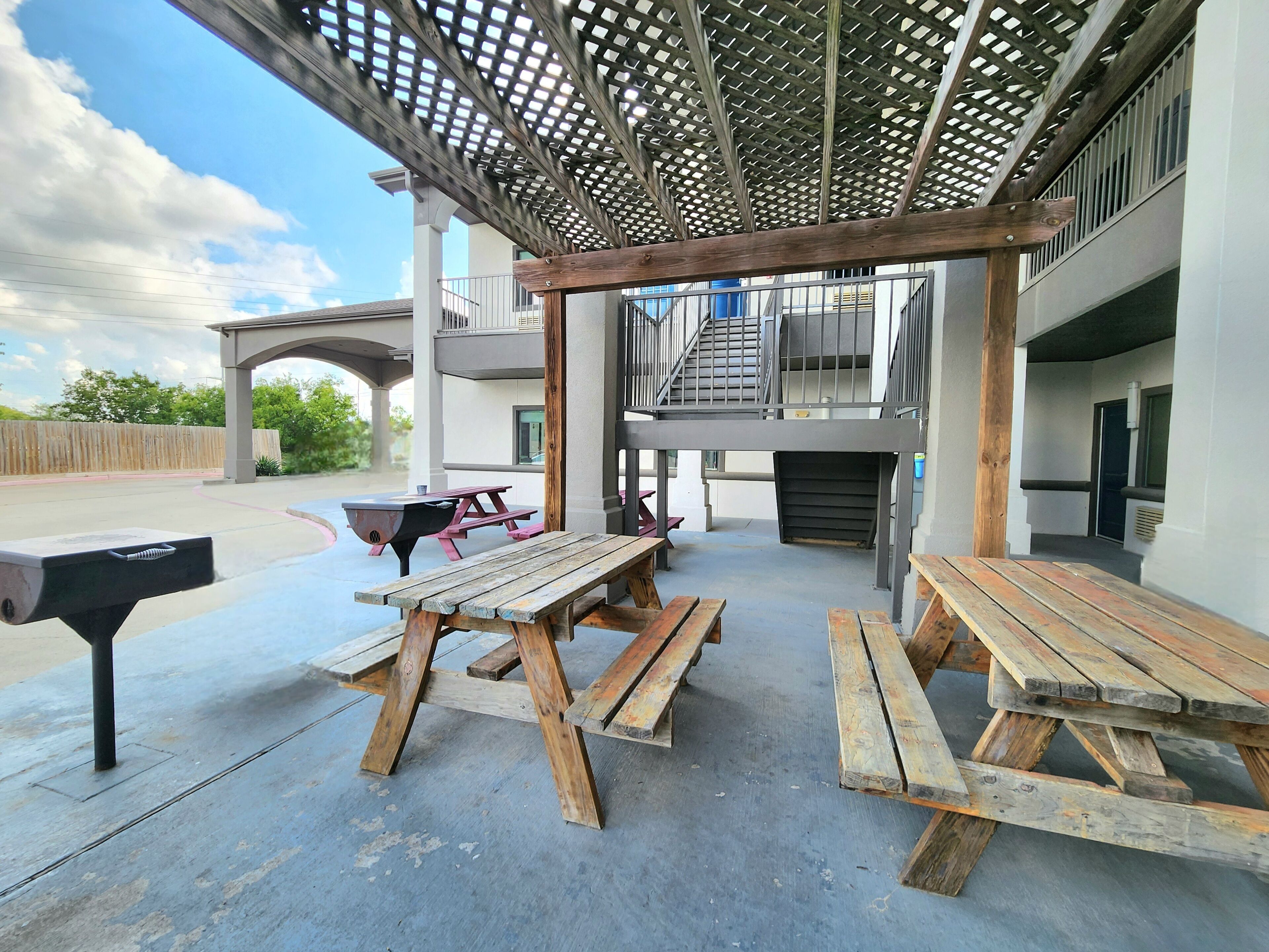 An outdoor patio area with wooden picnic tables and a barbecue grill.