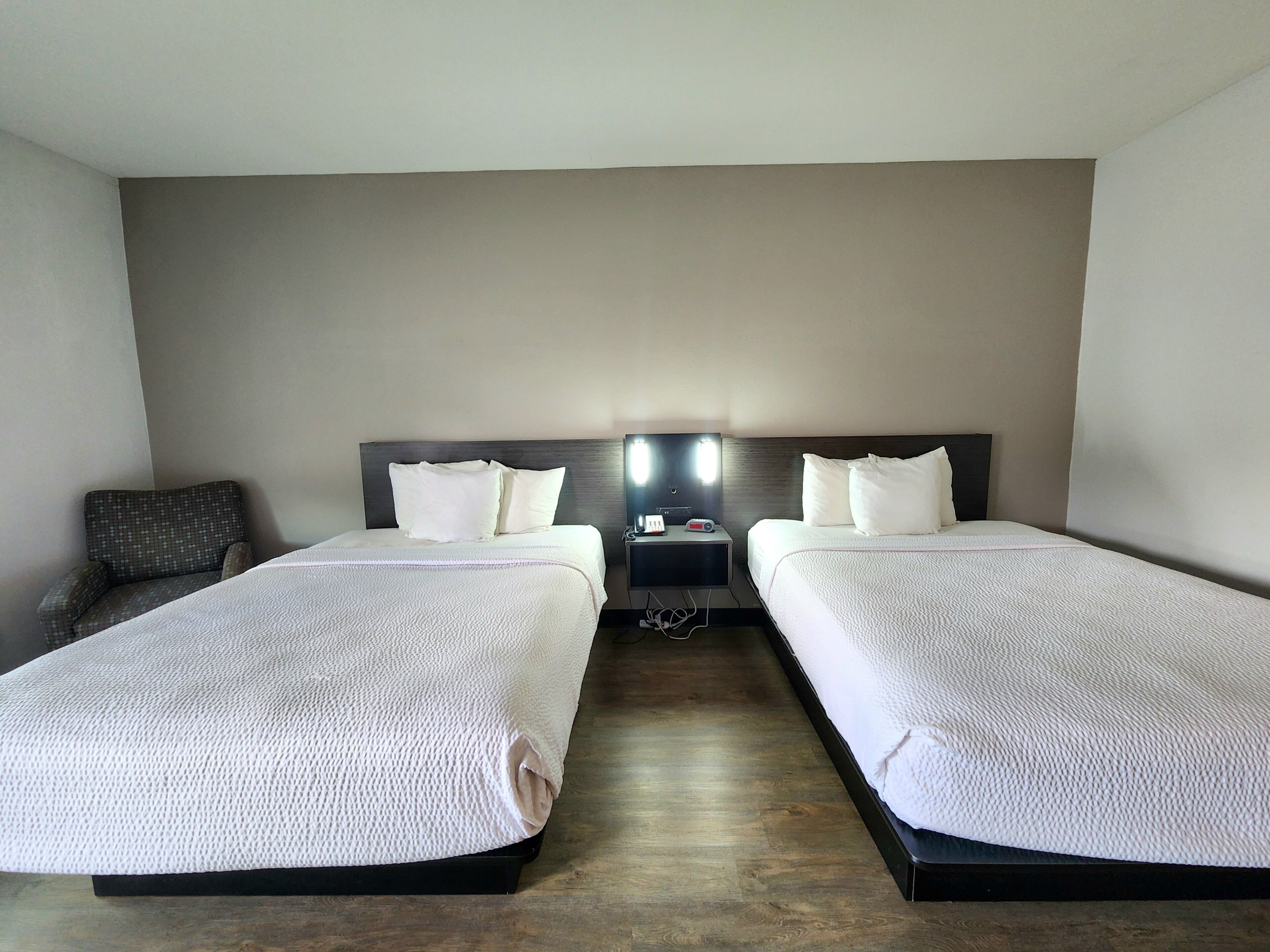 A hotel room with two beds, a nightstand, and a chair.
