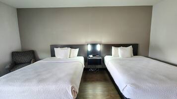 A hotel room with two beds, a nightstand, and a chair.