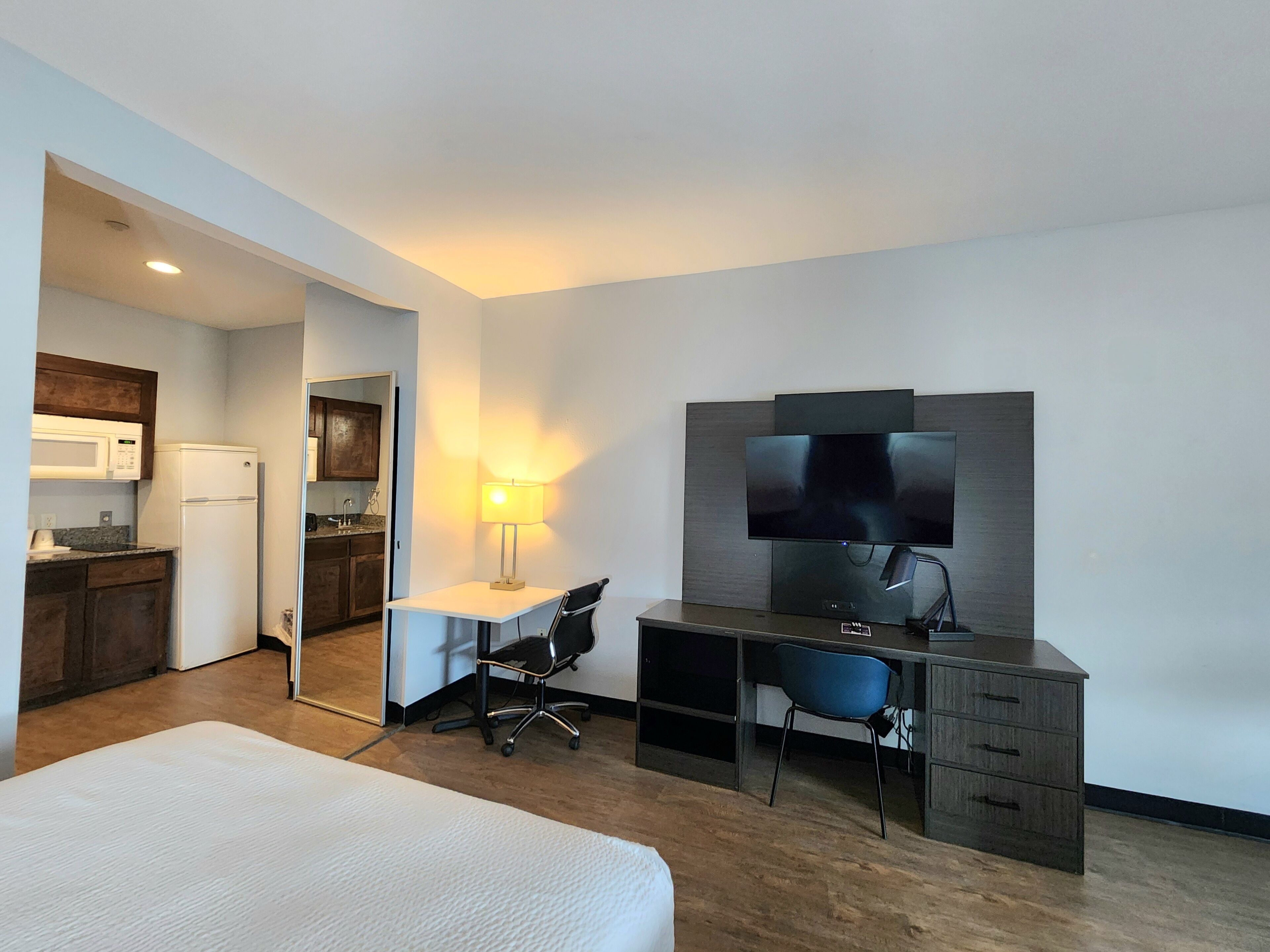 A hotel room with a bed, desk, chair, TV, and kitchenette.