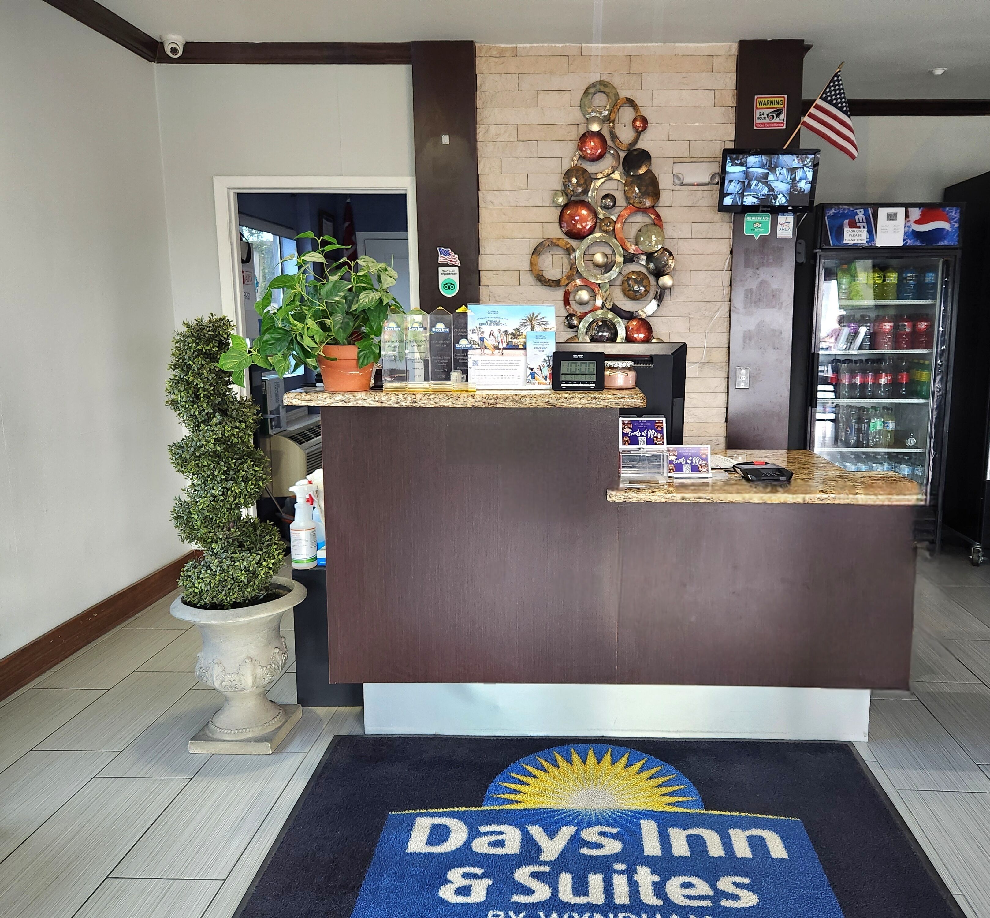 A reception desk with a digital screen, a plant, and a 'Days Inn & Suites' mat.