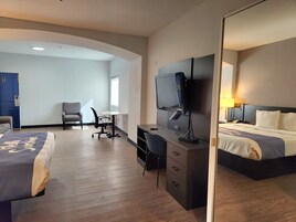 A hotel room with a bed, desk, chair, television, and a door.
