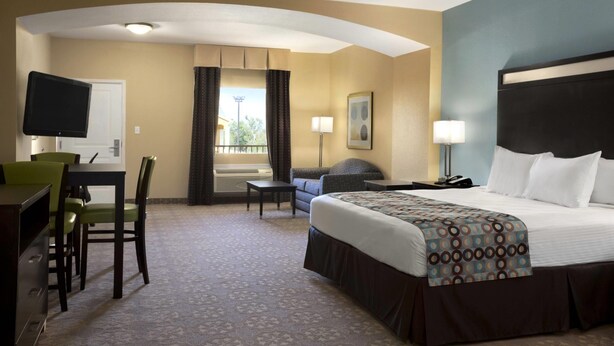 Habitación de hotel con cama, escritorio, sillas, televisor y ventana con cortinas.