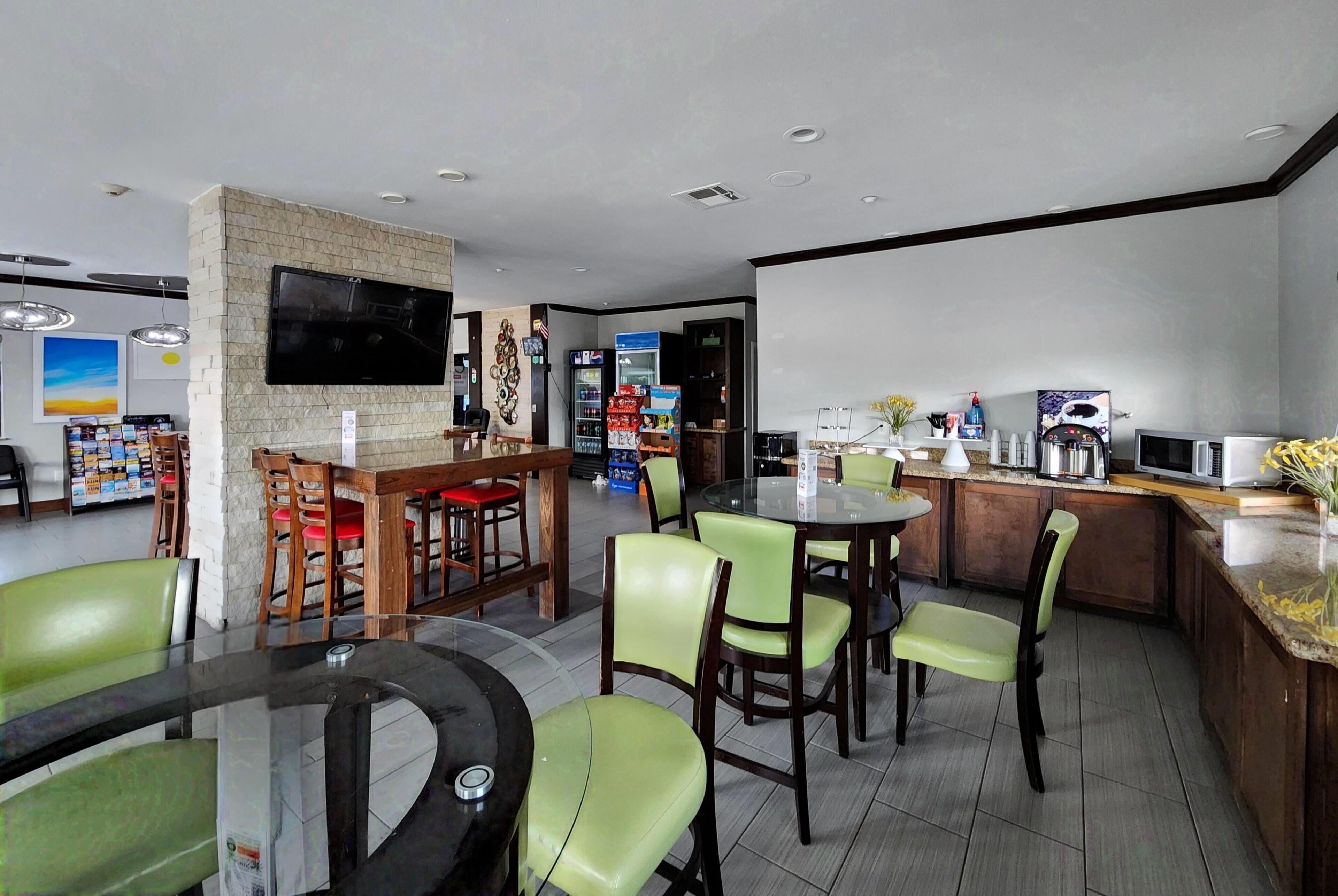 A modern restaurant with a bar area, multiple seating options including round tables and booths, and a flat-screen TV mounted on the wall.