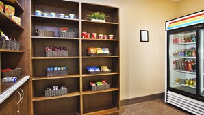 Habitación de hotel con un mueble para aperitivos repleto de distintos productos y un refrigerador para bebidas.