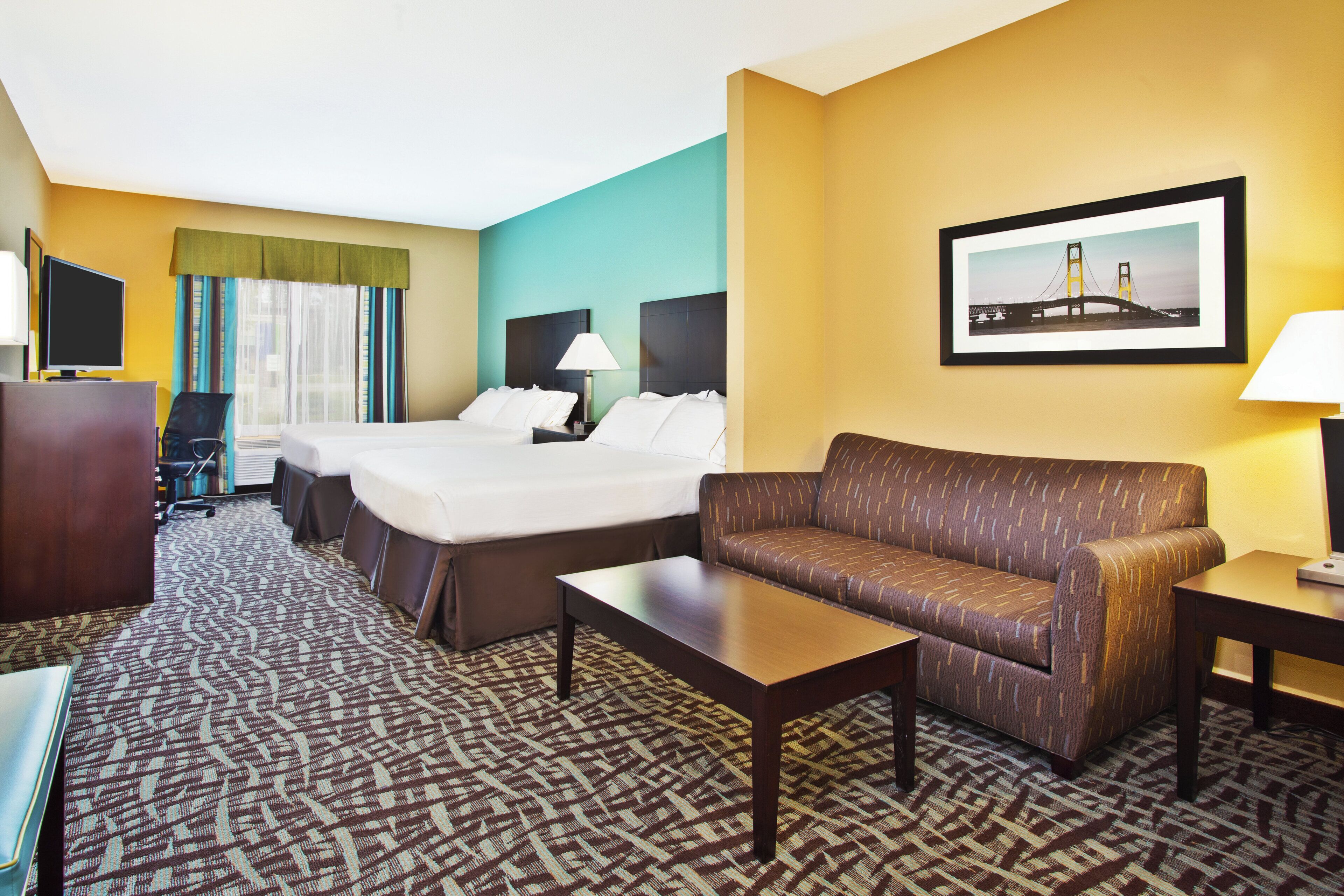 A hotel room with a bed, a sofa, a desk, a TV, and a framed picture on the wall.