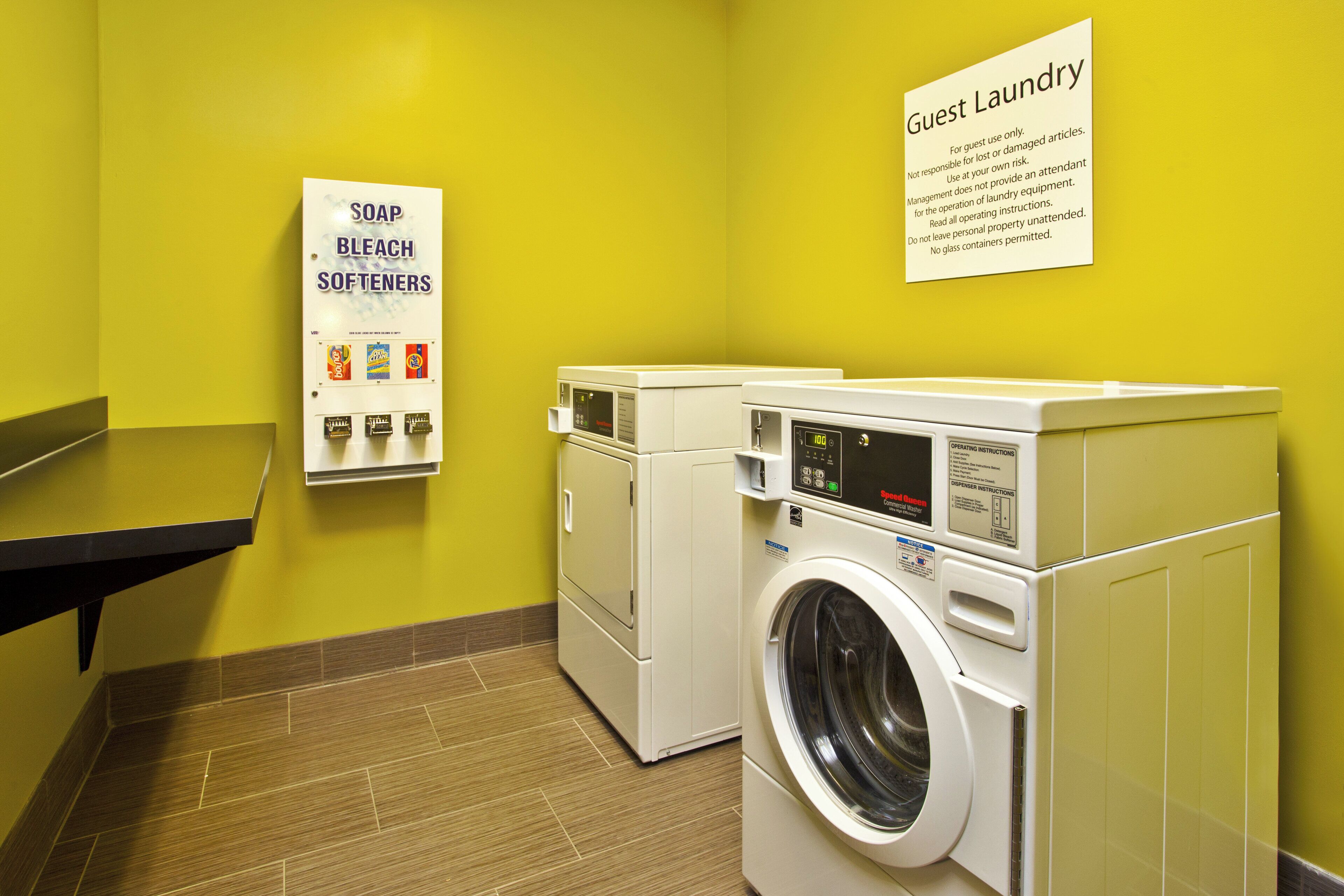 A laundry area with a sign indicating guest use, a soap and bleach softener dispenser, and a front-loading washing machine.